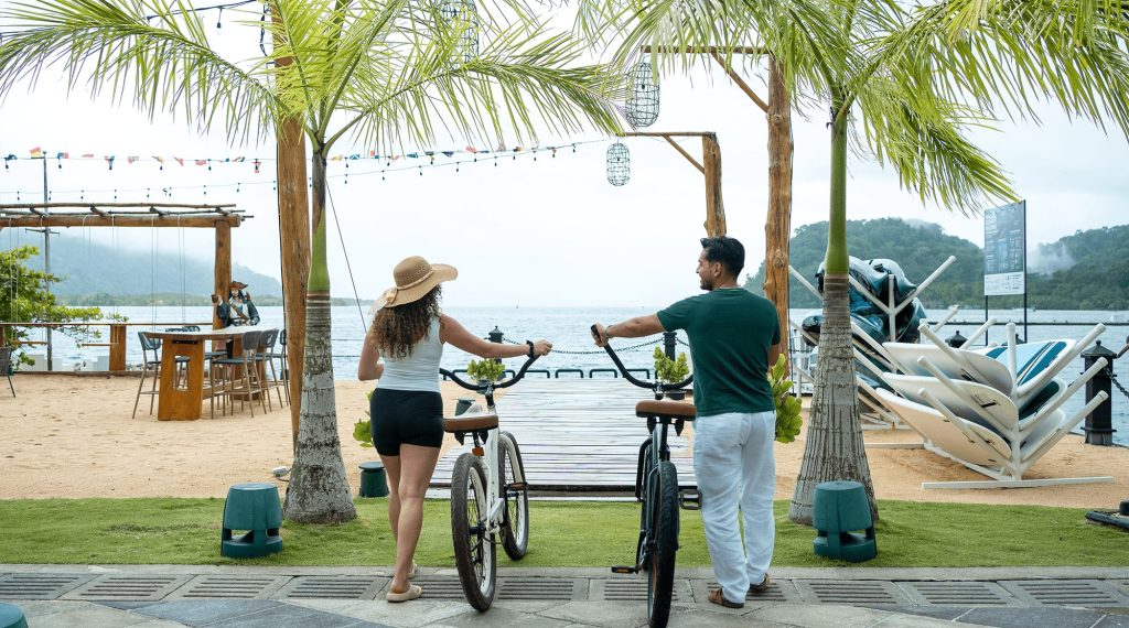 Couple with bicycles at the Marina Village waterfront in Golfito, Costa Rica, looking out toward the dock.