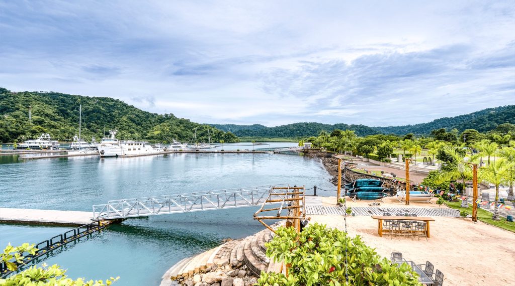 Panoramic view of Marina Bahia Golfito with docked yachts, waterfront beach club, and jungle-covered hills on Costa Rica's southern Pacific coast.