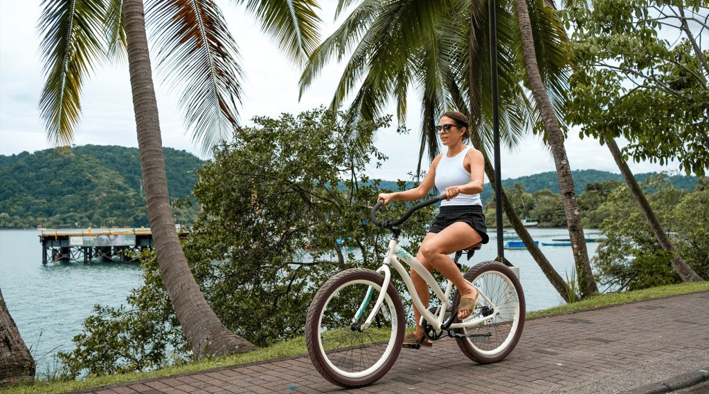 Woman cycling a palm-lined waterfront path in Golfito, Costa Rica, with the protected gulf behind her