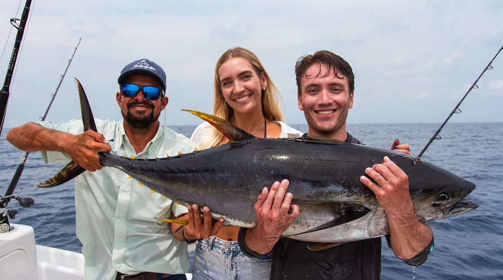 A captain and two anglers holding a large yellowfin tuna caught while sportfishing offshore of Golfito, Costa Rica.