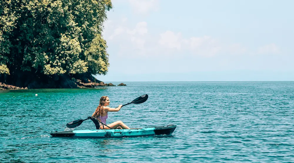 Woman kayaking the calm waters of the Golfo Dulce near Golfito, Costa Rica, with rainforest shoreline behind her