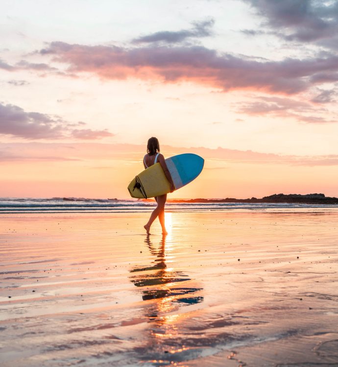Surfer carrying board at sunset on Southern Zone beach, Golfito Costa Rica